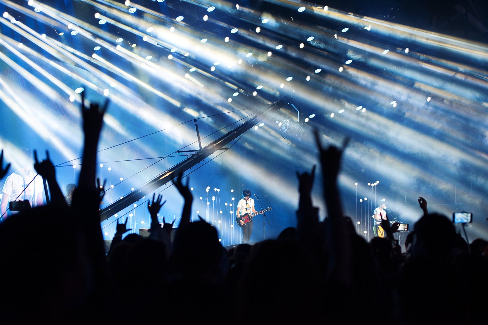 Rockkoncert kék fénycsóvákkal, a közönség feltartott kezekkel, a zenekar a színpadon